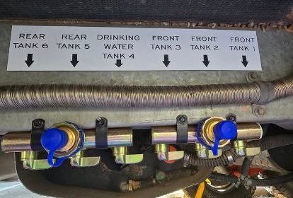 Underneath this caravan we see a closeup showing 7 different water storage outlets for fresh and grey water, labelled by the owner for covenience