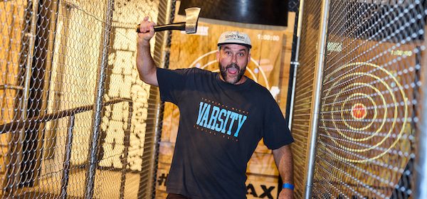 A man holding up an Axe ready to throw an axe in a indoor sporting lane divided with cyclone fencing each side at a Maniax venue